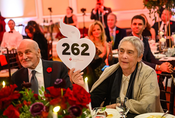 Seated woman holding up bidder paddle number 262.